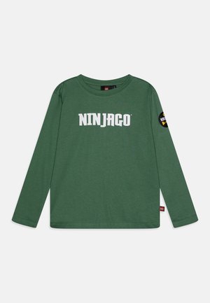 Zelené tričko s dlouhým rukávem vyrobené z měkké bavlny, s výrazným nápisem "NINJAGO" v bílých písmenech a kulatou nášivkou na levém rukávu.