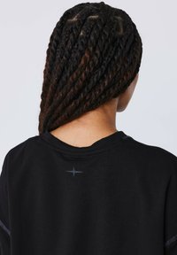 T-shirt nera con vestibilità rilassata, caratterizzata da un sottile dettaglio riflettente a forma di stella sulla parte posteriore del collo e capelli intrecciati testurizzati.