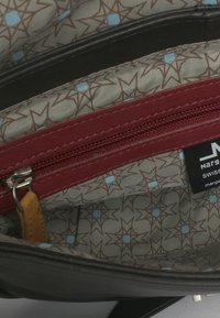 Interno di una borsa in pelle nera con rivestimento in tessuto grigio caratterizzato da motivi a stella in marrone e blu. Tasca con zip rossa e etichetta del marchio visibili.