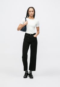 Czarne jeansy z wysokim stanem z subtelnymi wzorami, zestawione z dopasowanym białym t-shirtem. Do tego ciemnoniebieska torba i błyszczące czarne buty.