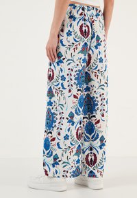 Witte broek met bloemmotief in blauw, rood en groen, met een losse pasvorm en een elastische tailleband. Gecombineerd met witte sneakers.