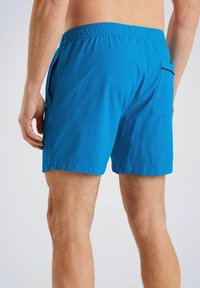 Shorts de bain bleus en tissu doux et léger, avec une taille élastique et une poche arrière unique. Texture lisse, longueur jusqu'au milieu de la cuisse.