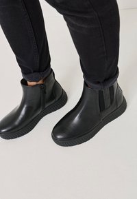 Botine negre până la gleznă, din piele netedă, cu fermoar lateral, panou elastic și talpă din cauciuc texturat cu modele în relief.