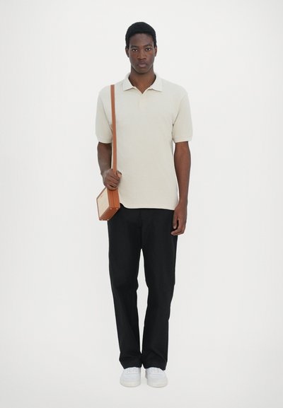Polo beige, pantalon noir, baskets blanches et un petit sac bandoulière marron. Tissu lisse, coupe décontractée et design minimal.