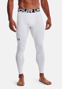 Biele športové legíny s čiernym elastickým pásom s nápisom "UNDER ARMOUR." Vyrobené z hladkého, elastického materiálu, priliehajúceho na telo.