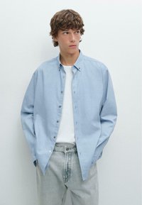 Hellblaues Hemd mit Knöpfen aus weichem Stoff, mit Kragen und langen Ärmeln, kombiniert mit hellgrauen Jeans.