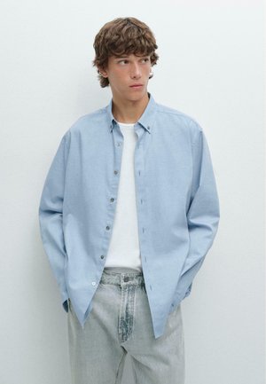 Lichtblauw overhemdd-shirt van zacht materiaal, met een kraag en lange mouwen, gecombineerd met lichtgrijze denim jeans.