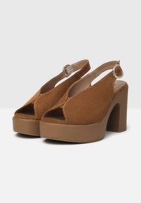 Talons plateformes en suede marron avec un bout ouvert, un design découpé et une bride de cheville avec une boucle argentée. Talon bloc épais.