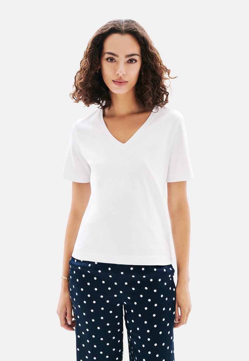 Witte korte mouwen V-hals t-shirt gemaakt van een gladde stof, gedragen met marineblauwe broek met stippen, met een ontspannen pasvorm en subtiele stikseldetails.