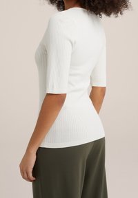 Ribbad vit tröja med korta ärmar, figurnära design, texturerad tyg och rundad halsringning, tillsammans med mörkgröna byxor.