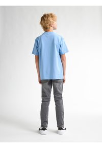 Camiseta de algodón azul con mangas cortas, ajuste relajado, combinada con jeans gris ajustados y zapatillas en blanco y negro. Diseño sencillo sin patrones.