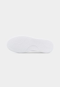 Λευκή σόλα παπουτσιού από καουτσούκ με υφή σχέδιο λαβής και καμπυλωτή εγκοπή στη μέση σε ανοιχτό γκρι φόντο.