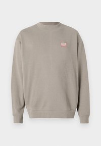 Lys grå sweatshirt laget av myk stoff med ribbet rund hals og mansjetter. Har et lite rød og hvit logo-lapp på brystet.