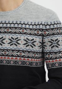 Strickpullover mit grauem Körper, schwarzen und blauen geometrischen Mustern, roten Akzenten und einem gerippten Ausschnitt. Dunkler unterer Bereich.
