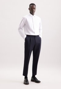 Camicia bianca con bottone, pantaloni blu scuro e scarpe nere stringate. Tessuto liscio, vestibilità su misura e design classico con linee pulite.