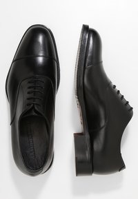 Chaussures habillées en cuir noir avec un bout arrondi, design à lacets, texture lisse et petit talon empilé. Accents de couture minimalistes visibles.