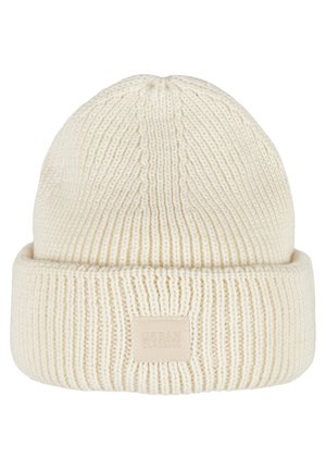 Cream knitted beanie with a folded brim, featuring vertical ribbing and a stitched brand label on the front. Soft texture.