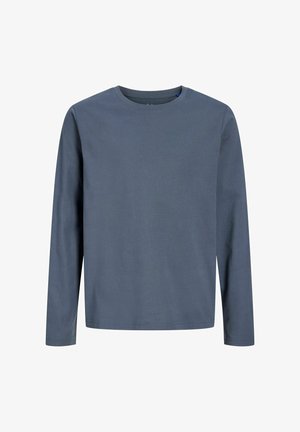 Poiss seisab, vaadates otse ette, seljas sinise pikema varrukaga särk, laiad mustad püksid ja must-valged tossud tavalise valge taustaga.