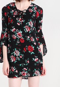 Musta kukallinen mekko, joka esittelee punaisia ja valkoisia ruusuja, solmittavan kaula-aukon ja kellohihat. Valmistettu kevyestä kankaasta, jossa on löysä istuvuus.