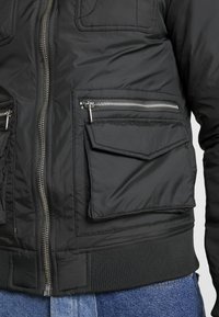 Svart pufferjacka med dragkedja fram, ribbade ärmslut och midja. Har två dragkedjefickor på sidorna och en fackficka på bröstet.