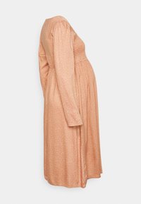 Vestido de maternidade em tecido pêssego suave com bolinhas brancas, apresentando mangas compridas, um corpete justo e um design de saia evasê.