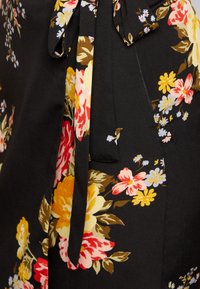 Tecido preto com uma estampa floral em amarelo, rosa e branco. Apresenta um detalhe amarrado e uma textura suave. Destaca-se pelas cores vibrantes e pelo design.