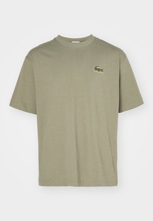 T-shirt en coton vert olive avec un col rond, des manches courtes et un petit logo de crocodile brodé sur la poitrine. Design simple, texture douce.