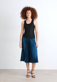 Top nero senza maniche in tessuto testurizzato abbinato a una gonna plissettata teal a lunghezza ginocchio e sandali neri con cinturini. Design semplice e moderno.