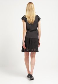 Top in satin nero con maniche corte a campana abbinato a una gonna nera con fori a occhio, indossato con scarpe nere.