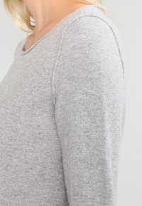 Jasnoszary sweter wykonany z miękkiego dzianiny, z okrągłym dekoltem i długimi rękawami z widocznymi detalami szwów.