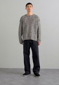 Multicolored knit sweater with a loose fit, patterned texture, and ribbed cuffs, paired with dark jeans and black sneakers.