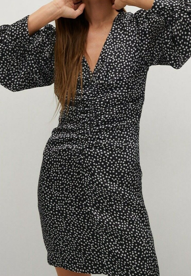 Robe noire à pois blancs, avec un décolleté en V, un design froncé et de longues manches bouffantes. Fabriquée en tissu léger, longueur genoux.