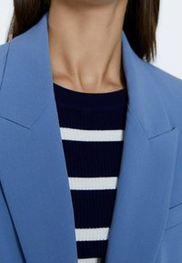 Ljusblå skräddarsydd blazer med skarpa slag, bärs över en marinrandig tröja. Slät tyg med en strukturerad design.