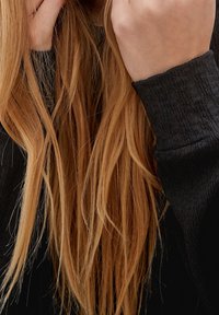 Suéter de tela texturizada negra con puños ajustados, combinado con cabello largo y lacio de color castaño claro que cae sobre los hombros.