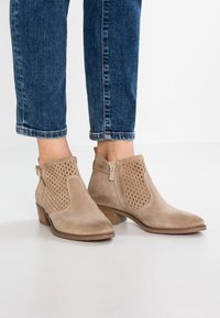 Beige mokkanahkasaappaat, joissa on rei'itetty kuvio, matala pinottu korko ja sivuvetoketju, yhdistettynä lyhyisiin sinisiin farkkuihin.