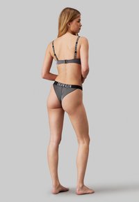 Crni i sivi prugasti bikini s podešivim trakama. Sadrži Calvin Klein logo na pojasu. Glatka tekstura, usklađen dizajn, minimalna pokrivenost.