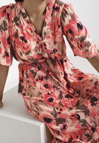 Robe fleurie dans des tons de rose, corail et noir. Comprend des manches courtes, un décolleté en V et une taille cintrée, réalisée en tissu léger.
