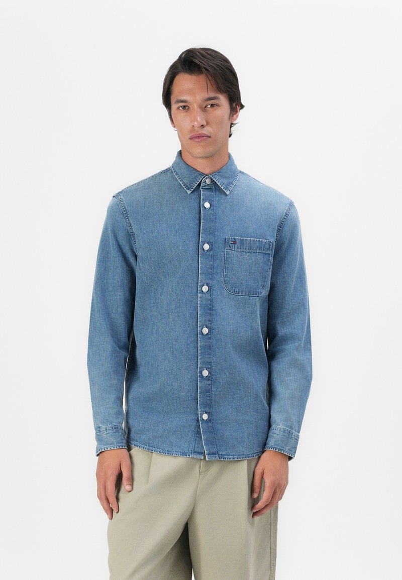 Lichtblauwe spijkerblouse met een button-down kraag, borstzak en logodetail. Lange mouwen en een relaxte pasvorm. Glad textuur.