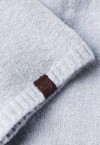 Heled hall villane särk, millel on tekstuuriline muster, ning mille varrukal on pruunist nahast silt, millel on karu logo. Pehme villane materjal.