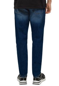 Dunkelblaue Denim-Jeans mit geradem Bein, sichtbaren Gesäßtaschen und leichter Ausbleichung. Kombiniert mit schwarz-weißen Sneakern.