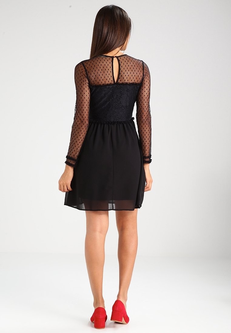 Black dress with sheer polka dot sleeves, lace bodice, and a flared, lightweight skirt. Red heels complete the outfit.