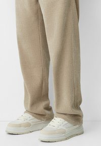 Pantalones de canalé beige con un corte holgado, combinados con zapatillas chunky blancas y beige que presentan una parte superior texturizada y una suela acolchada.
