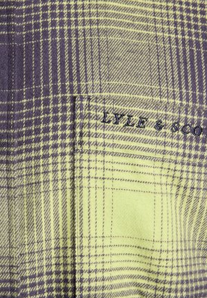 Plaid fabric in green and purple, with a smooth texture. Features a pocket and embroidered "LYLE & SCOTT" logo in dark thread.