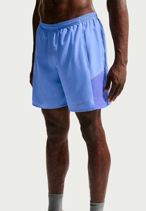 Mandlig torso og ben iført lyseblå atletikshorts med mesh sidepaneler og grå ankelstrømper mod en ensfarvet baggrund.