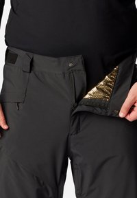Schwarze isolierte Hose mit einer Reißverschlusstasche und goldfarbener reflektierender Innenauskleidung. Enthält verstellbare Träger und einen Druckknopfverschluss an der Taille.