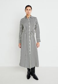 Čiernobiele pruhované šaty s gombíkmi, ktoré majú opasok v páse, dlhé rukávy a kontrastné pruhované manžety. Materiál sa zdá byť ľahký.