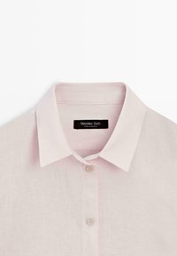 Světle růžová lněná košile s klasickým límečkem a dvěma bílými knoflíky viditelnými na přední straně, označená Massimo Dutti, vyrobená v Maroku.
