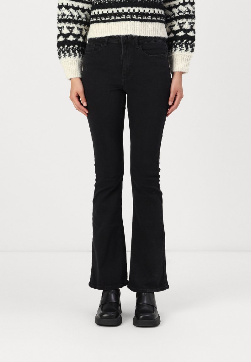 Melni platā kāja džinsi, izgatavoti no denima, izceļas ar klasisku piecu kabatu dizainu un pieguļošu jostasvietu. Kombinēti ar rakstainu džemperi un stilīgām melnām kurpēm.