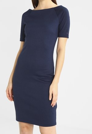 Granatowa dopasowana sukienka z krótkimi rękawami, dekoltem w łódkę i gładkim materiałem. Na lewym rękawie znajduje się delikatne logo.