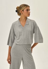 Szary krótki sweter z dekoltem w serek, krótkimi szerokimi rękawami i miękką fakturą. Połączony z szarymi spodniami o luźnym kroju i elastycznym pasie.